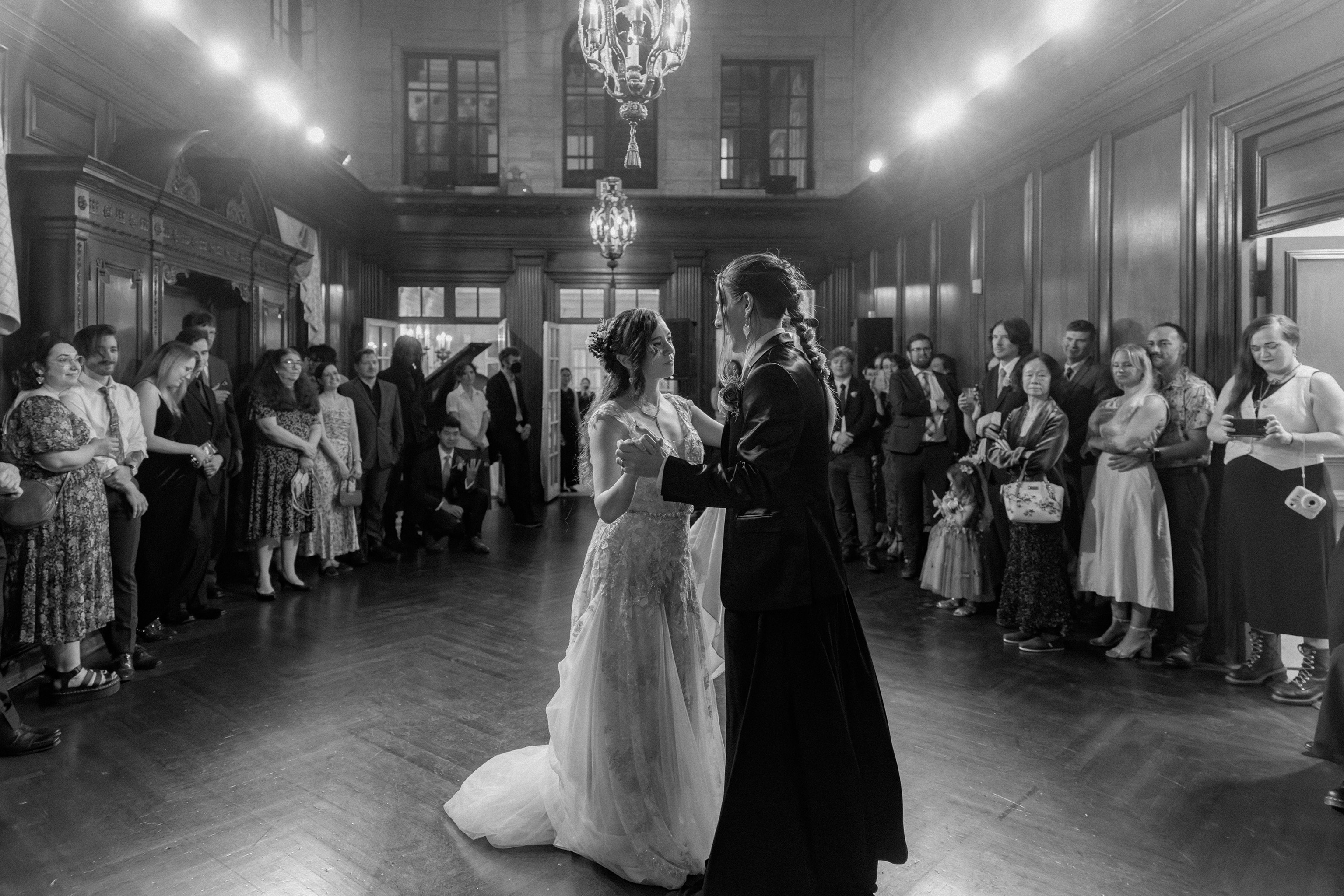 Dramatic black and white reception photo of guests dancing in a grand ballroom